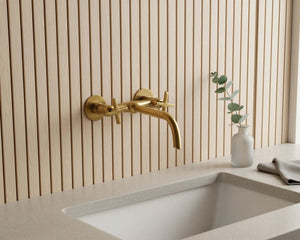 Gold faucet on a modern kitchen sink with a neutral wall background