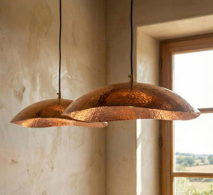Two copper pendant lights hanging in a room with a window in the background.