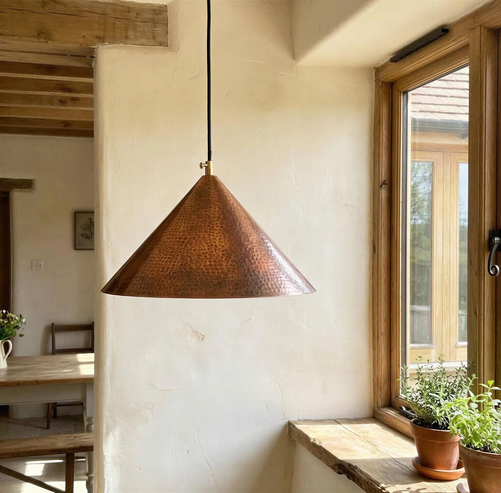Copper pendant light hanging in a room with wooden beams and a window.