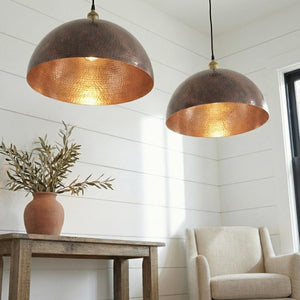 Two copper pendant lights hanging above a table with a plant and chair in a room.