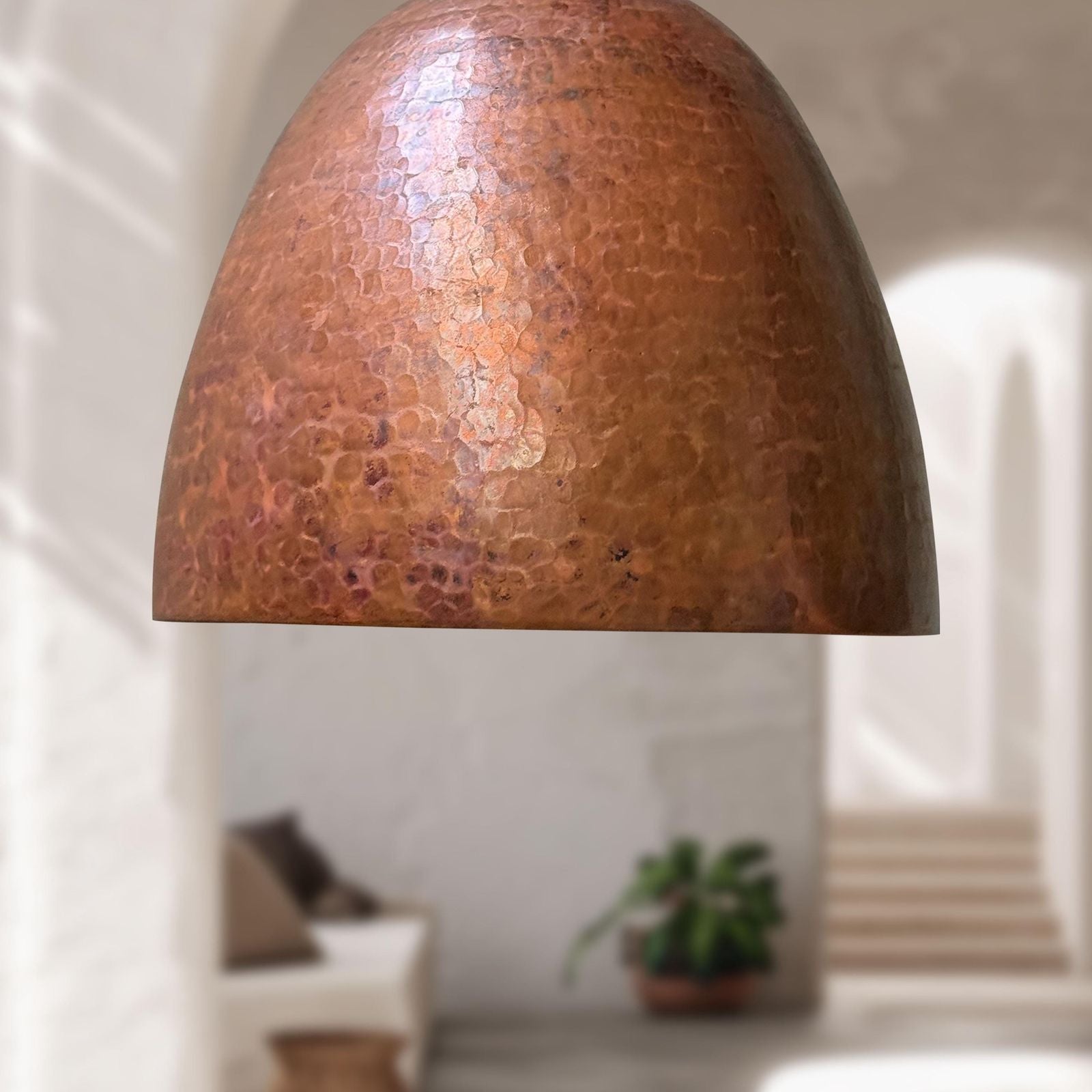 Copper pendant light fixture with a textured surface in a softly blurred room setting.