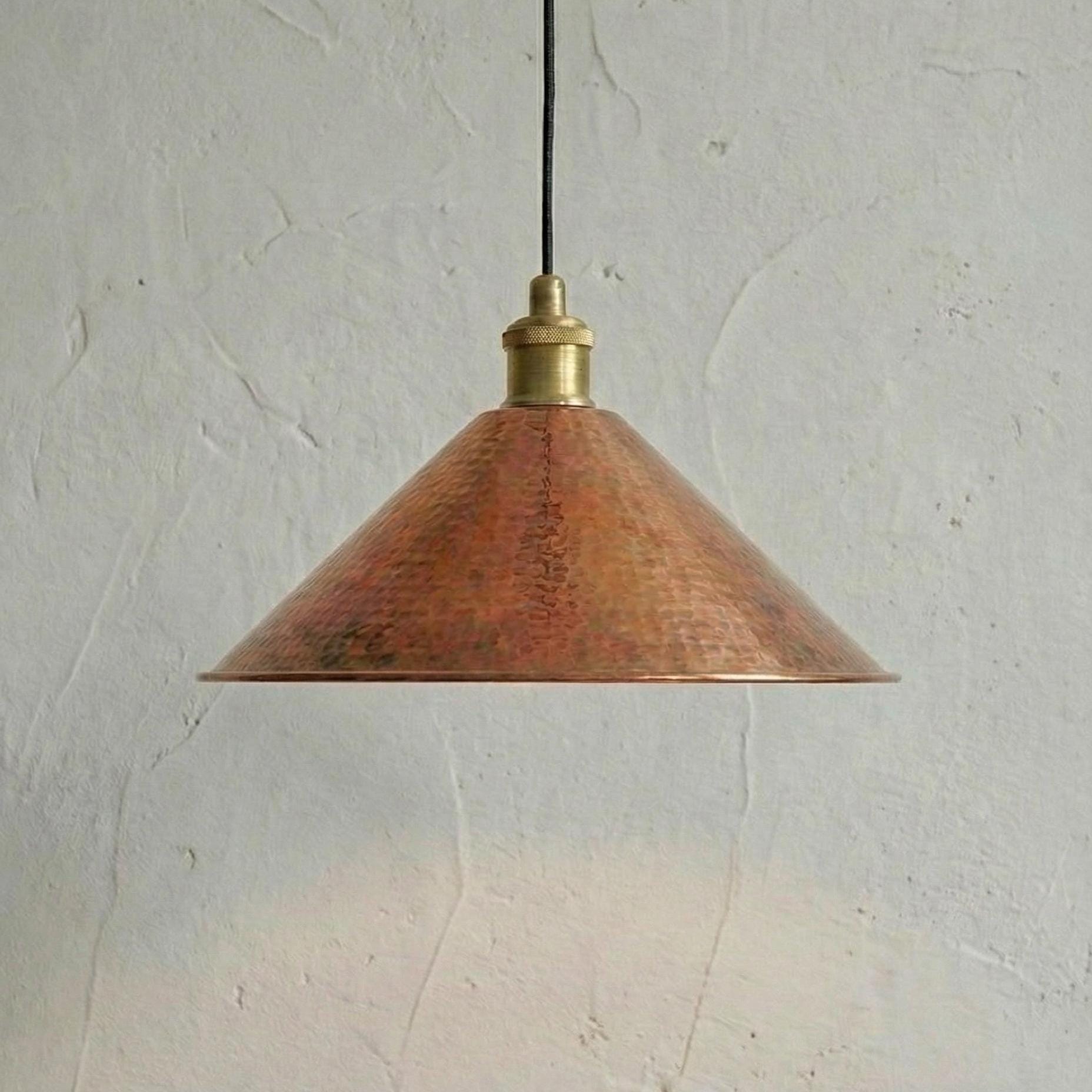 Copper pendant light with brass fitting against a textured white wall