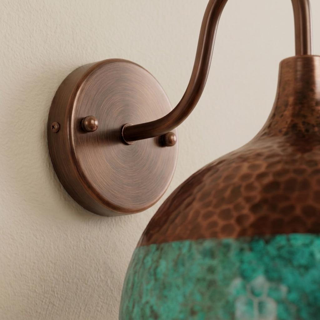 Close-up of a wall-mounted sconce with a round bronze backplate, curved bronze arm, and a hammered copper-toned shade transitioning into a textured turquoise lower section, mounted on a light beige wall.