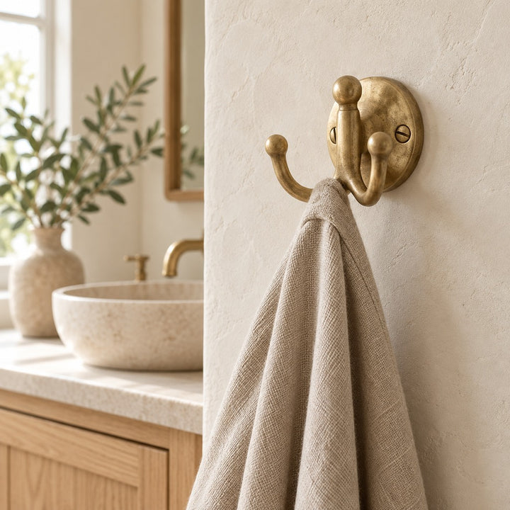 Vintage solid brass double robe hook with linen towel in a neutral bathroom