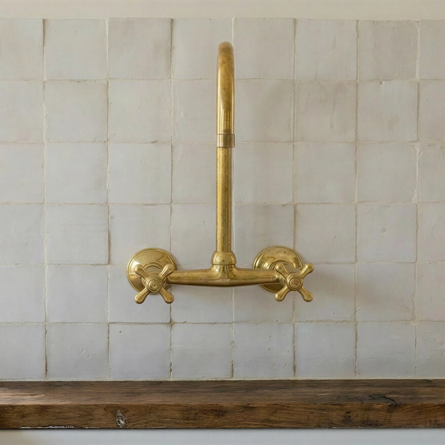 A vintage-style brass wall-mounted faucet with two cross handles, installed above a dark wood sink against a white tiled backsplash.