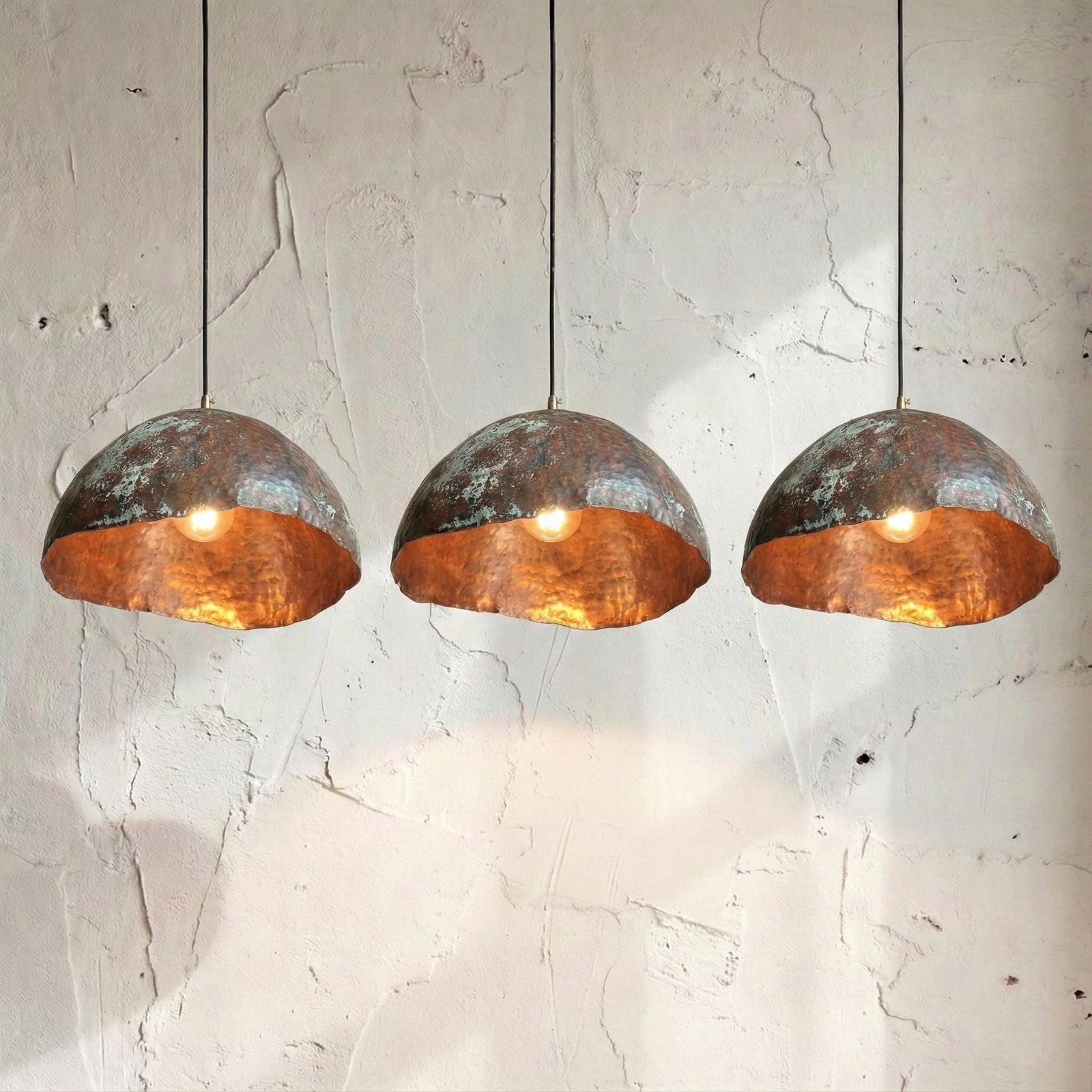 Three copper pendant lights hanging against a textured white wall.