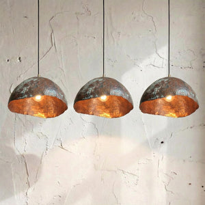 Three copper pendant lights hanging against a textured white wall.