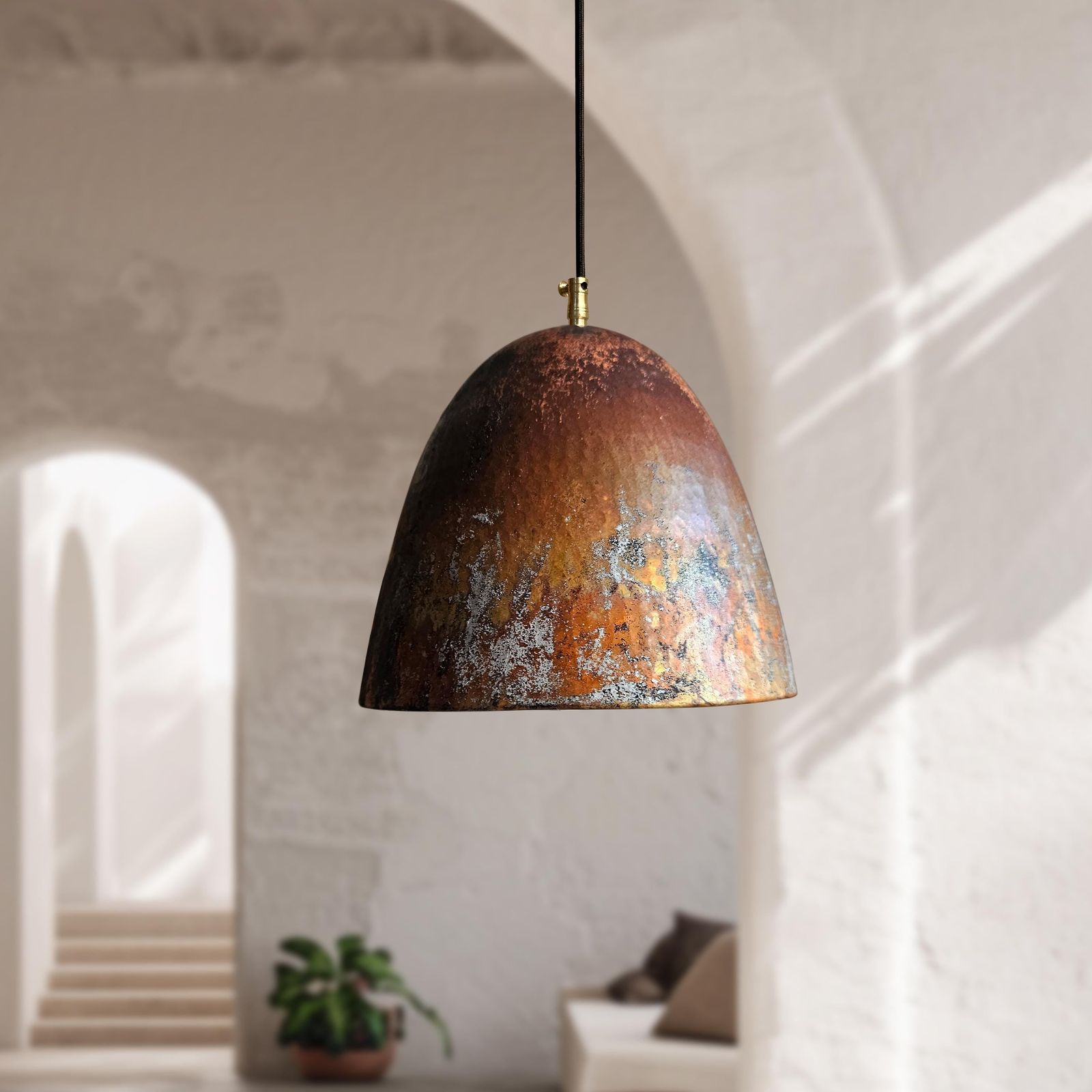 Rust-colored pendant light hanging in a room with white walls and a plant.